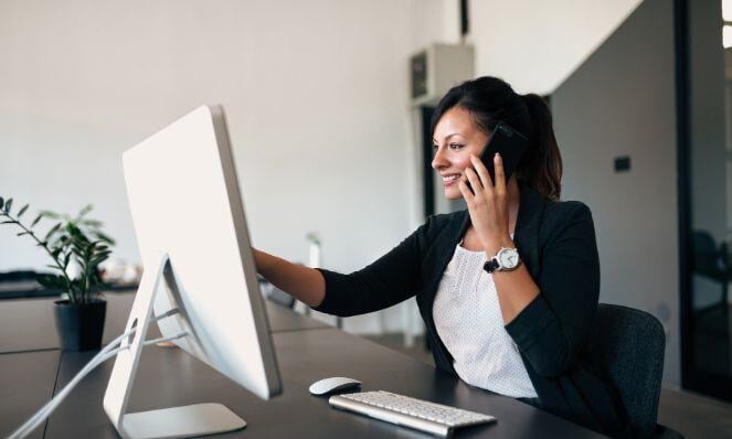 Account manager working on her computer while talking on her phone.