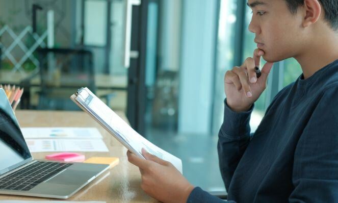 A young man is looking at a document and assessing information.