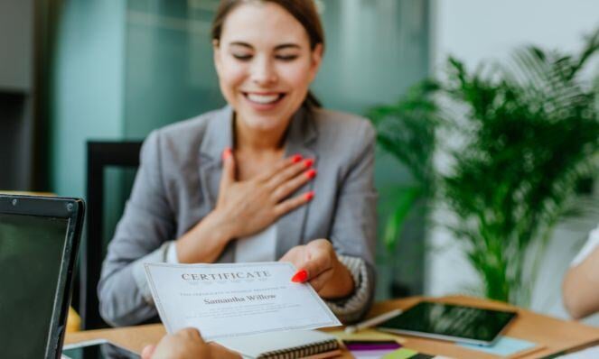 Woman smiling as she is handed a certification with her name on it.