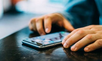 A man has a cell phone sitting on a table. The cell phone screen shows social apps.