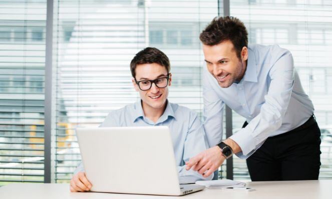 Two men working together while looking at a laptop screen.