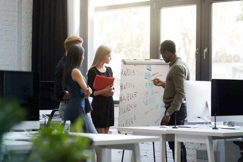 A group of employee collaborating and talking about the writings on the white board.