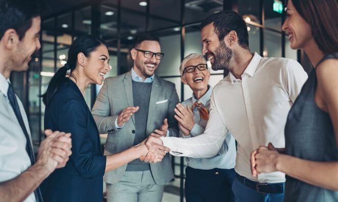 Professional people gathered together shaking hands and smiling.