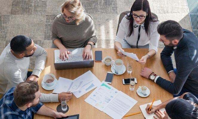 Workmates working together and collaborating; holding papers and talking to each other.