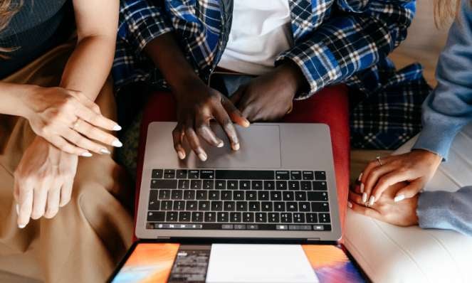 Three people seated in front of a laptop, only their hands and arms are visible.