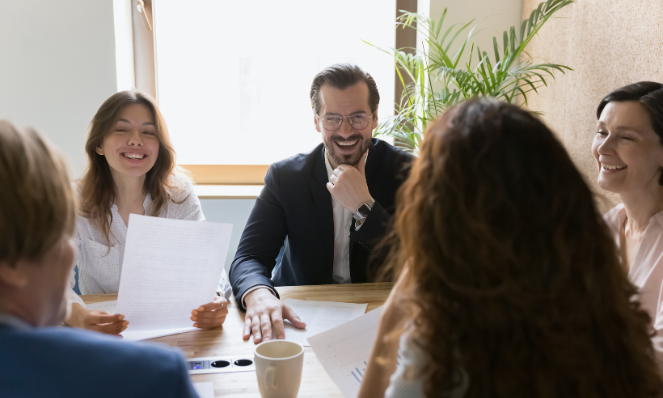 Five people are seated around a table. They are smiling and looking over paperwork together.