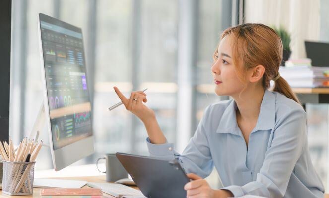 A woman is looking at her monitor with charts and data.