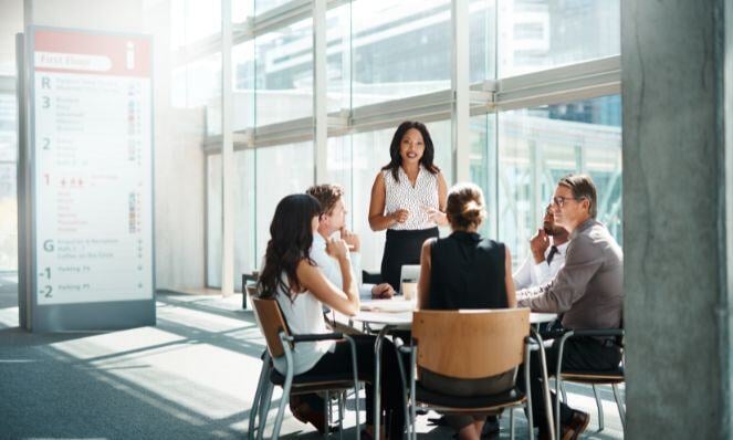 Workmates gathered together having an important meeting while seated around a table in a room with floor to ceiling windows.