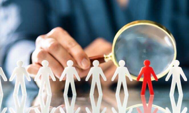 Person focusing their magnifying glass on a small, colorful human figurines.