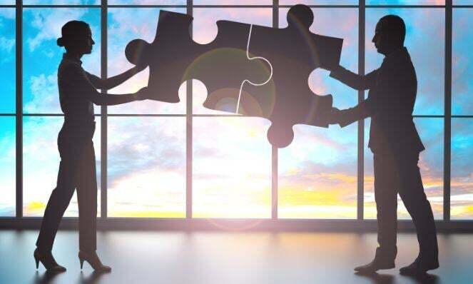 Silhouette of two people piecing a puzzle together.