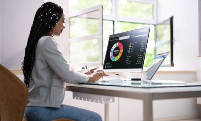 A woman is working at her computer with a pie chart showing on her monitor.